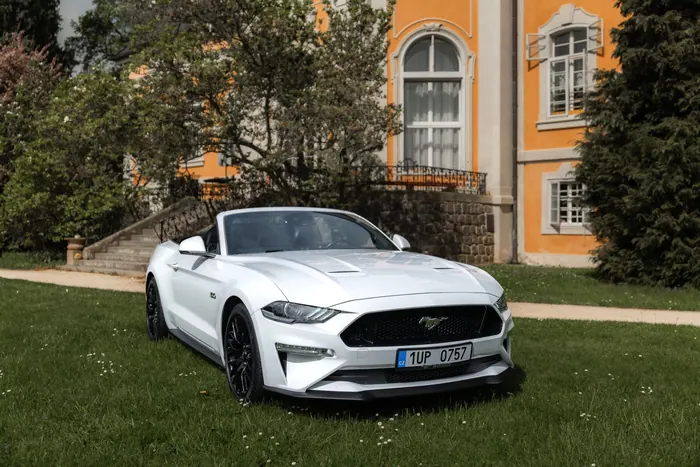 Bílý Ford Mustang GT Cabrio zaparkovaný před historickou budovou